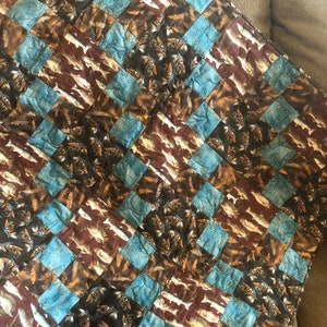 May include: A quilt with a checkered pattern featuring a brown and blue fabric with a fish print.