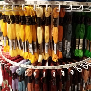 May include: A close-up of a rotating display stand filled with colorful embroidery floss spools. The spools are organized by color and numbered. The numbers on the stand range from 234 to 359.