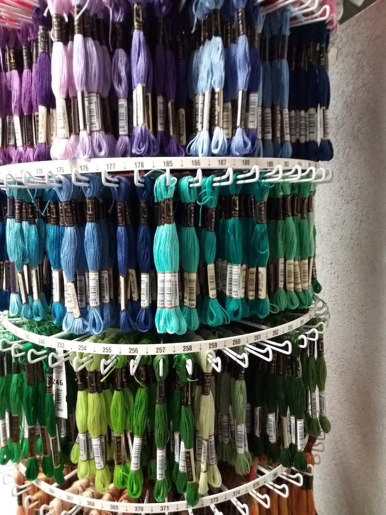 May include: A close-up of a rotating display stand filled with spools of embroidery floss. The floss is organized by color and numbered. The numbers range from 170 to 375.