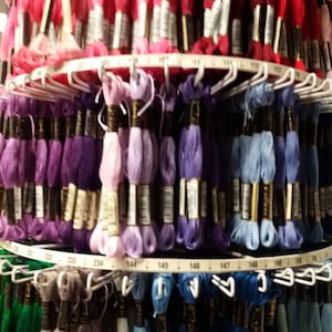 May include: A close-up of a large spool of embroidery floss with different colors of thread. The floss is organized by color and number. The numbers are visible on the spool.