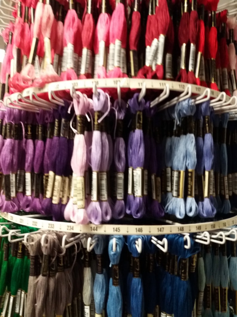 May include: A close-up of a large spool of embroidery floss with different colors of thread. The floss is organized by color and number. The numbers are visible on the spool.