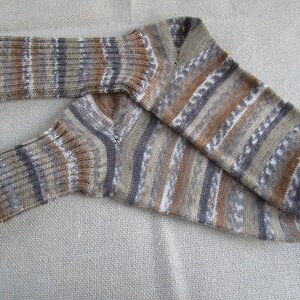 Könnte beinhalten: Ein Paar gestreifte Socken in Braun, Grau und Weiß mit einem Strickmuster. Die Socken sind in der Mitte gefaltet und liegen auf einer beigefarbenen Stoffoberfläche.