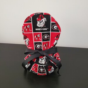 May include: Red and black scrub hat with a University of Georgia logo and bulldog mascot. The hat is tied with a black ribbon.