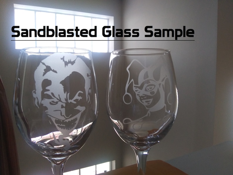May include: Two clear glass wine glasses with sandblasted designs. The glass on the left features a white silhouette of the Joker, while the glass on the right features a white silhouette of Harley Quinn.