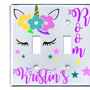 May include: A white light switch cover with a unicorn design. The unicorn has a rainbow mane and tail, and is surrounded by stars. The text "Kristin's Room" is written in purple on the cover.