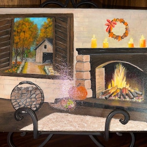 May include: A rectangular painting depicts a cozy indoor scene with a stone fireplace featuring a bright orange fire. A window shows an autumn landscape with trees and a barn. A wreath, candles, a pumpkin, and a log holder are visible.