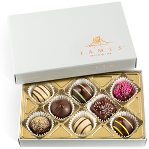 May include: A white box of assorted chocolates with gold foil dividers. The box lid features the text "FAMES Brooklyn 1948" and a bridge graphic. The chocolates are in white paper cups and have various toppings and designs.