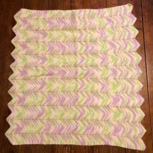 May include: A crocheted baby blanket in a chevron pattern with shades of pink, green, and white.