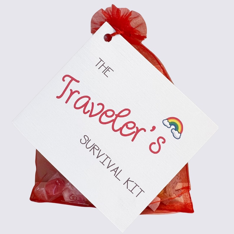 May include: A red mesh bag tied with a red ribbon, holding small items. A white tag is attached, with the words "The Traveler's Survival Kit" in red script and a rainbow graphic.