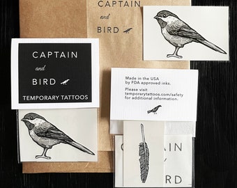 May include: A set of temporary tattoos featuring black and white illustrations of a bird and a feather. The packaging includes the text "Captain and Bird Temporary Tattoos" and information about the product being made in the USA with FDA approved inks.
