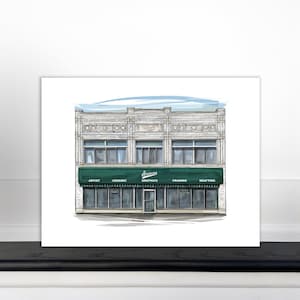May include: A hand-drawn illustration of a storefront with a green awning that reads "Green's Graphics". The storefront has a brick facade with large windows and a sign that reads "Artist, Ceramic, Framing, Drafting".