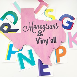 May include: Pink wooden cutout of the state of Texas with the text "Monograms & Vinyl'all" in black lettering. The cutout is surrounded by colorful letters and shapes.