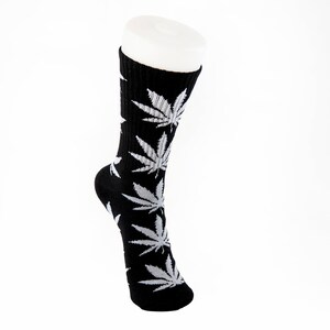 May include: Black socks with a repeating pattern of white cannabis leaves. The socks are displayed on a white mannequin foot against a white background. The socks are made of a soft, comfortable material.
