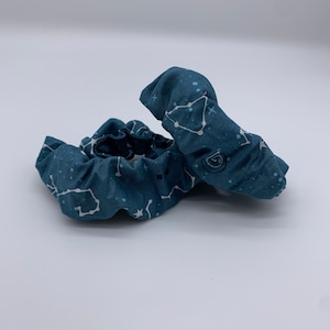 May include: Two dark blue fabric scrunchies with a white constellation pattern. The scrunchies are made of soft, stretchy fabric and are perfect for holding hair in place.
