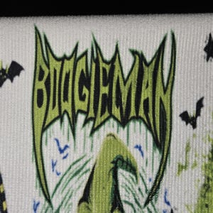 Puede incluir: Tela blanca con la palabra "BIGGHEMAN" en letras verdes estilizadas. El dise&ntilde;o incluye murci&eacute;lagos y estrellas, con una ilustraci&oacute;n verde y negra en la parte inferior. El tema general es Halloween.