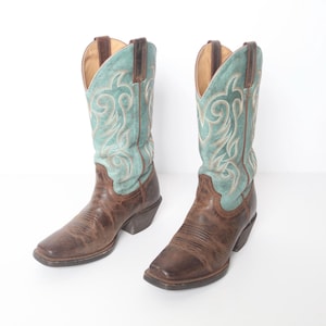 May include: A pair of brown leather cowboy boots with turquoise embroidery. The boots have a pointed toe and a low heel.