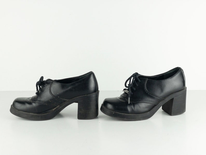 May include: A pair of black leather platform shoes with lace-up closures. The shoes have a chunky heel and a rounded toe.
