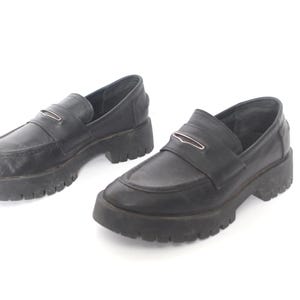 May include: A pair of black leather loafers with a chunky platform sole. The loafers have a silver buckle detail on the vamp.