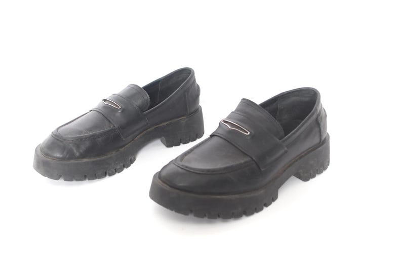 May include: A pair of black leather loafers with a chunky platform sole. The loafers have a silver buckle detail on the vamp.