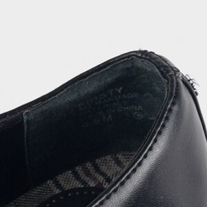 May include: Close-up of the inside of a black leather shoe with the text "BASTTY" and "MAN MADE MATERIALS" and "MADE IN CHINA" printed on the insole.