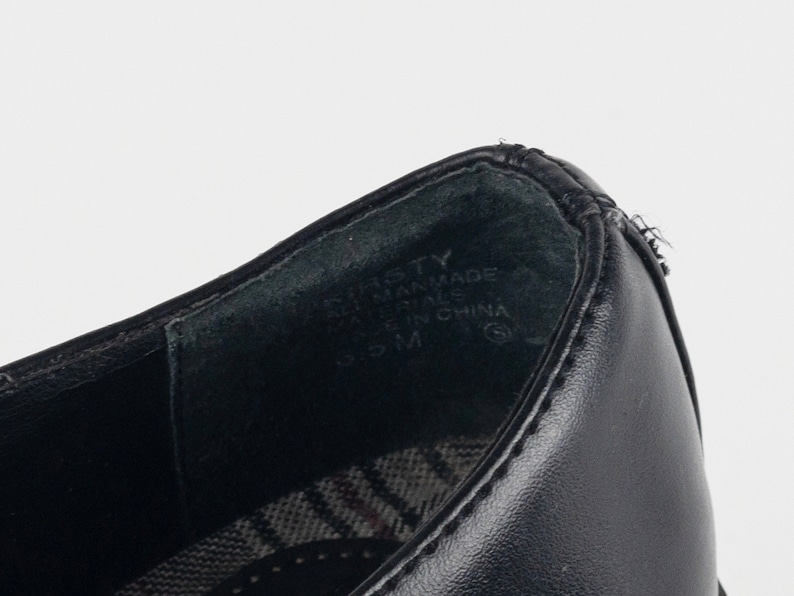 May include: Close-up of the inside of a black leather shoe with the text "BASTTY" and "MAN MADE MATERIALS" and "MADE IN CHINA" printed on the insole.