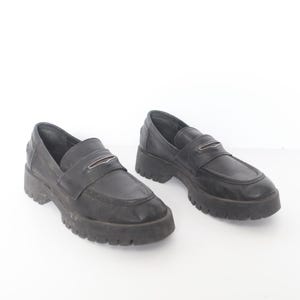May include: A pair of black leather loafers with a chunky platform sole. The loafers have a silver buckle detail on the front.