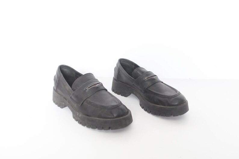 May include: A pair of black leather loafers with a chunky platform sole. The loafers have a silver buckle detail on the front.