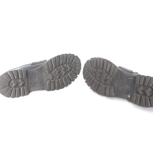 May include: A pair of black leather shoes with a textured rubber sole. The shoes are shown from the bottom, with the soles facing the camera.