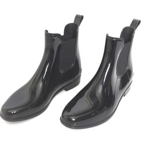 Puede incluir: Un par de botines negros brillantes. Estas botas de lluvia tienen una lengüeta en la parte trasera y paneles laterales elásticos. Las botas tienen un tacón bajo y una punta redondeada.