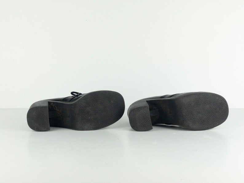 May include: A pair of black leather platform shoes with a chunky heel. The shoes have a lace-up front and a textured sole.