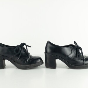May include: Pair of black leather heeled shoes with lace-up closures. The shoes have a chunky heel and a square toe.
