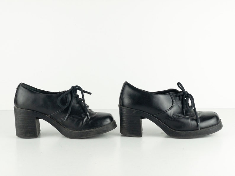 May include: Pair of black leather heeled shoes with lace-up closures. The shoes have a chunky heel and a square toe.