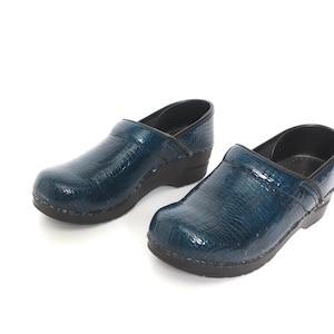 May include: A pair of blue leather clogs with a textured finish. The clogs have a black rubber sole and a closed toe.