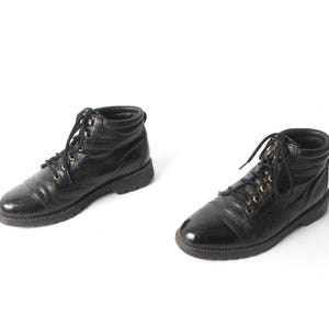 May include: A pair of black leather ankle boots with gold accents on the laces. The boots have a lace-up closure and a rounded toe.