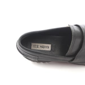 May include: Black leather loafers with a silver buckle and the text "Steve Madden" on the insole.
