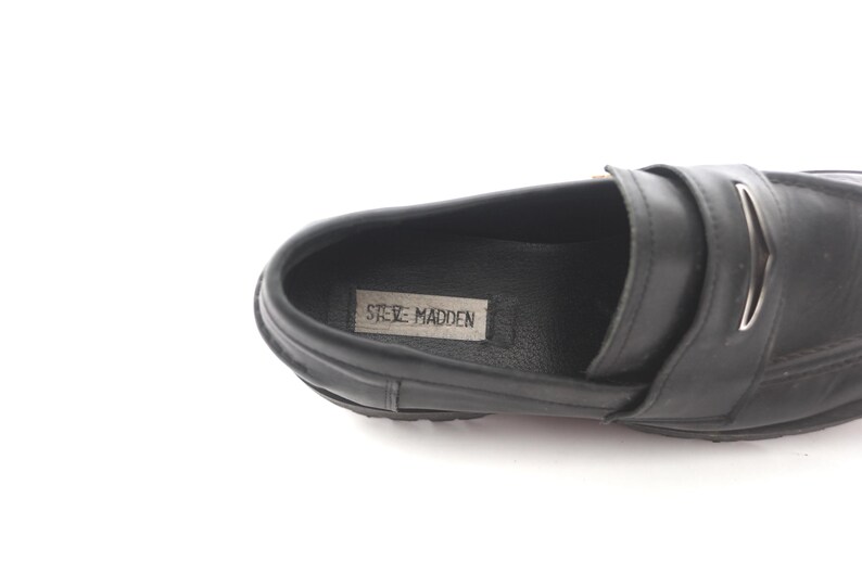 May include: Black leather loafers with a silver buckle and the text "Steve Madden" on the insole.