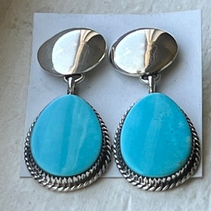 Può includere: Un paio di orecchini d'argento con pietre turchesi. Le pietre sono di colore blu chiaro e hanno un motivo a spirale. Gli orecchini hanno una forma a goccia e hanno un bordo argentato.