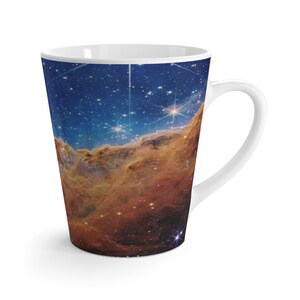 May include: A white ceramic mug with a handle features a colorful image of a nebula with stars and a blue background.