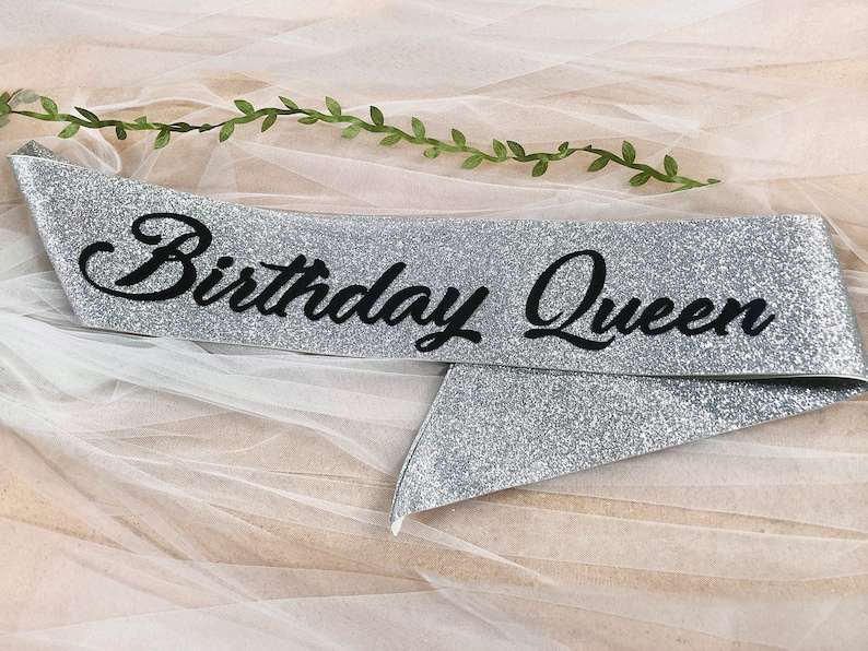 May include: Silver glitter sash with the text "Birthday Queen" in black cursive lettering.