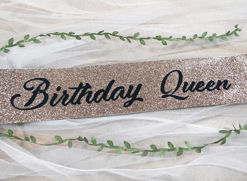 May include: A gold glitter sash with the text "Birthday Queen" in black cursive lettering.