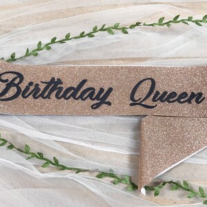 May include: A gold glitter sash with the text "Birthday Queen" in black lettering.