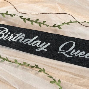 May include: Black sparkly sash with silver glitter lettering that reads "Birthday Queen".