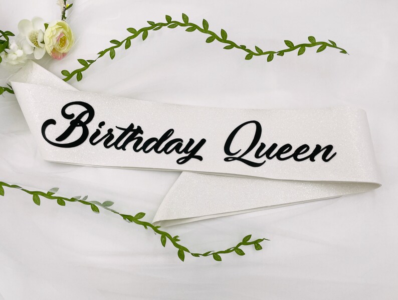 May include: White satin sash with black glitter lettering that reads "Birthday Queen".