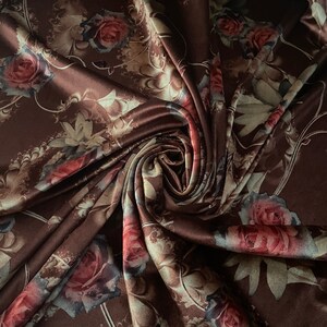 K&ouml;nnte beinhalten: Brauner Satin-Stoff mit einem Blumendruck mit Rosen und Bl&auml;ttern. Der Stoff ist drapiert und gefaltet und zeigt das komplizierte Design.