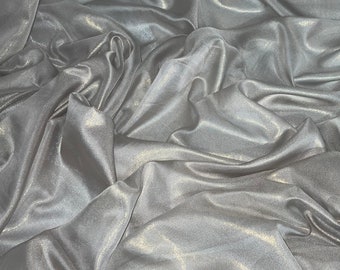 May include: A close-up of a silver fabric with a subtle shimmer. The fabric is draped and folded, creating soft, flowing lines.