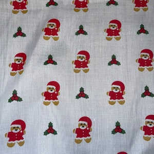 May include: White fabric with a repeating pattern of gingerbread men wearing Santa hats and holly sprigs.