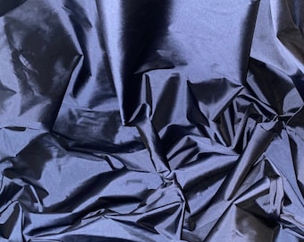 May include: A close-up of a dark blue fabric with a smooth, silky texture. The fabric is draped and folded, creating a soft and flowing look.