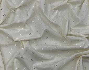May include: White cotton fabric with a delicate embroidered floral pattern. The fabric has a subtle sheen and a soft, drapey texture.