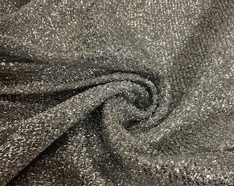 May include: Close-up of a silver sparkly fabric with a textured, woven pattern. The fabric is folded and draped, showing its shimmery texture.