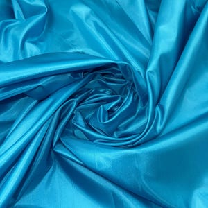 May include: A close-up of a vibrant turquoise fabric with a smooth, silky texture. The fabric is draped and folded, creating soft, flowing lines.